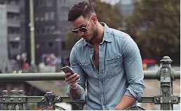 Hombre con camisa de denim y gafas de sol mirando su teléfono